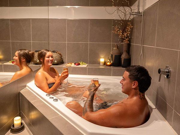 Couple enjoying a relaxing spa, surrounded bycandles and drinking champagne